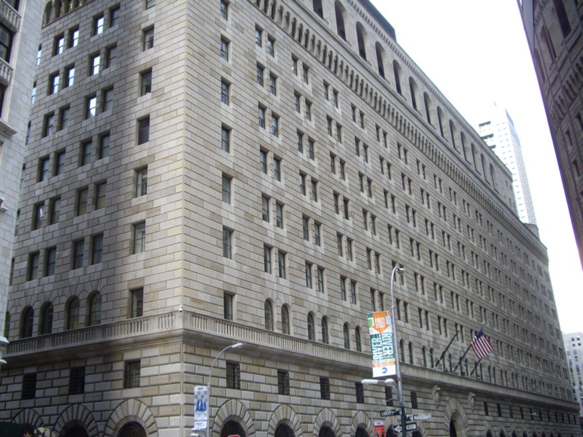 Exterior view of the Federal Reserve Bank of New York building at 33 Liberty Street, a large stone building with many windows and an American flag flying outside.