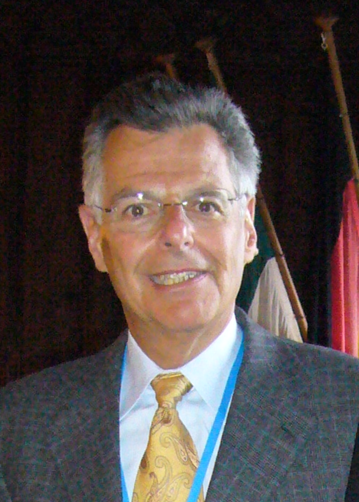 Portrait of Myron Scholes in 2008, wearing glasses, a patterned gold tie, and a blue lanyard.
