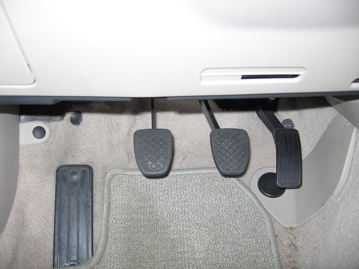 The footwell of a 2007 Subaru Legacy shows the automobile pedals from left to right: a foot rest, clutch, brake, and accelerator. The pedals are black with textured surfaces, set against a light-colored carpeted floor.