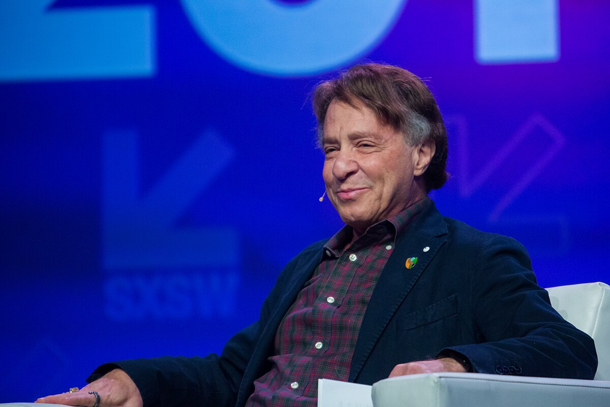 Ray Kurzweil smiling while seated on stage at SXSW 2017, wearing a plaid shirt and a dark jacket with a small pin on the lapel.