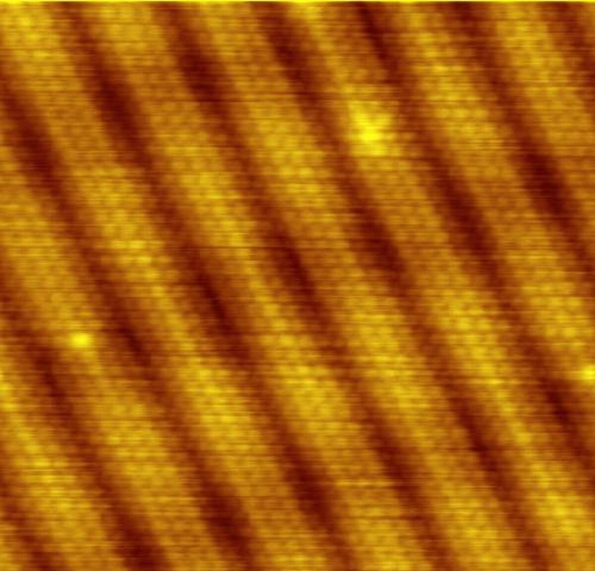 An atomic resolution scanning tunneling microscope image shows the reconstruction on a clean (100) surface of gold. The image displays a pattern of parallel ridges and valleys, indicating atomic-scale surface reconstruction.