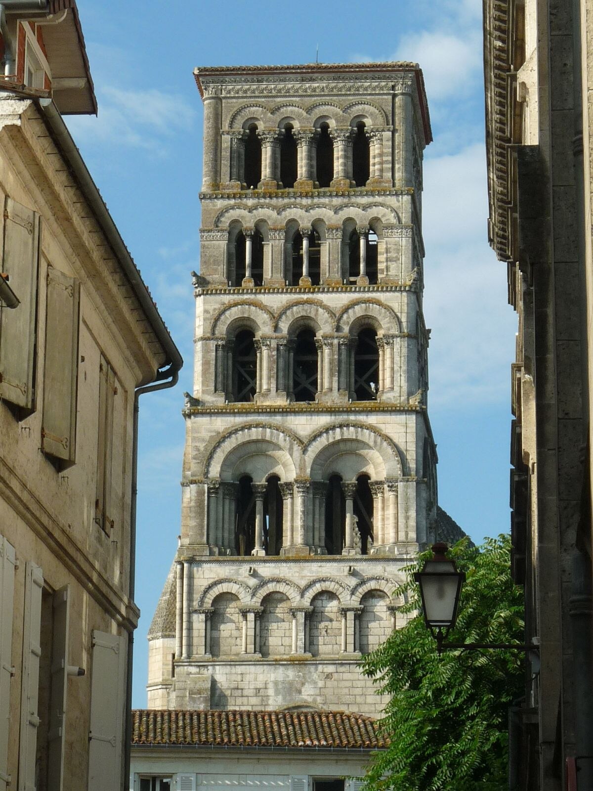 A tall, multi-tiered Romanesque bell tower with numerous arched openings, rising above surrounding buildings. The tower is constructed of light-colored stone and features decorative arcading.