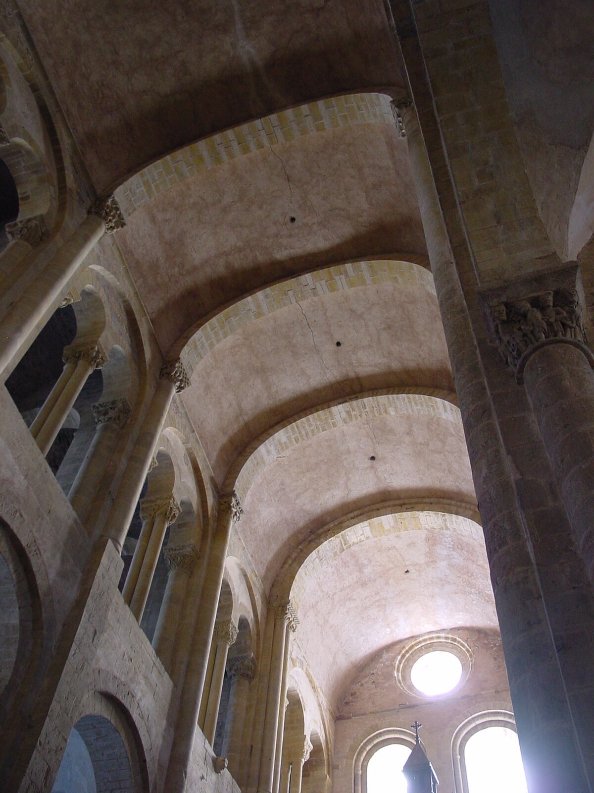 The interior of a Romanesque church, showing a barrel vault ceiling supported by thick columns and arches. Light enters through high windows, illuminating the stone structure.