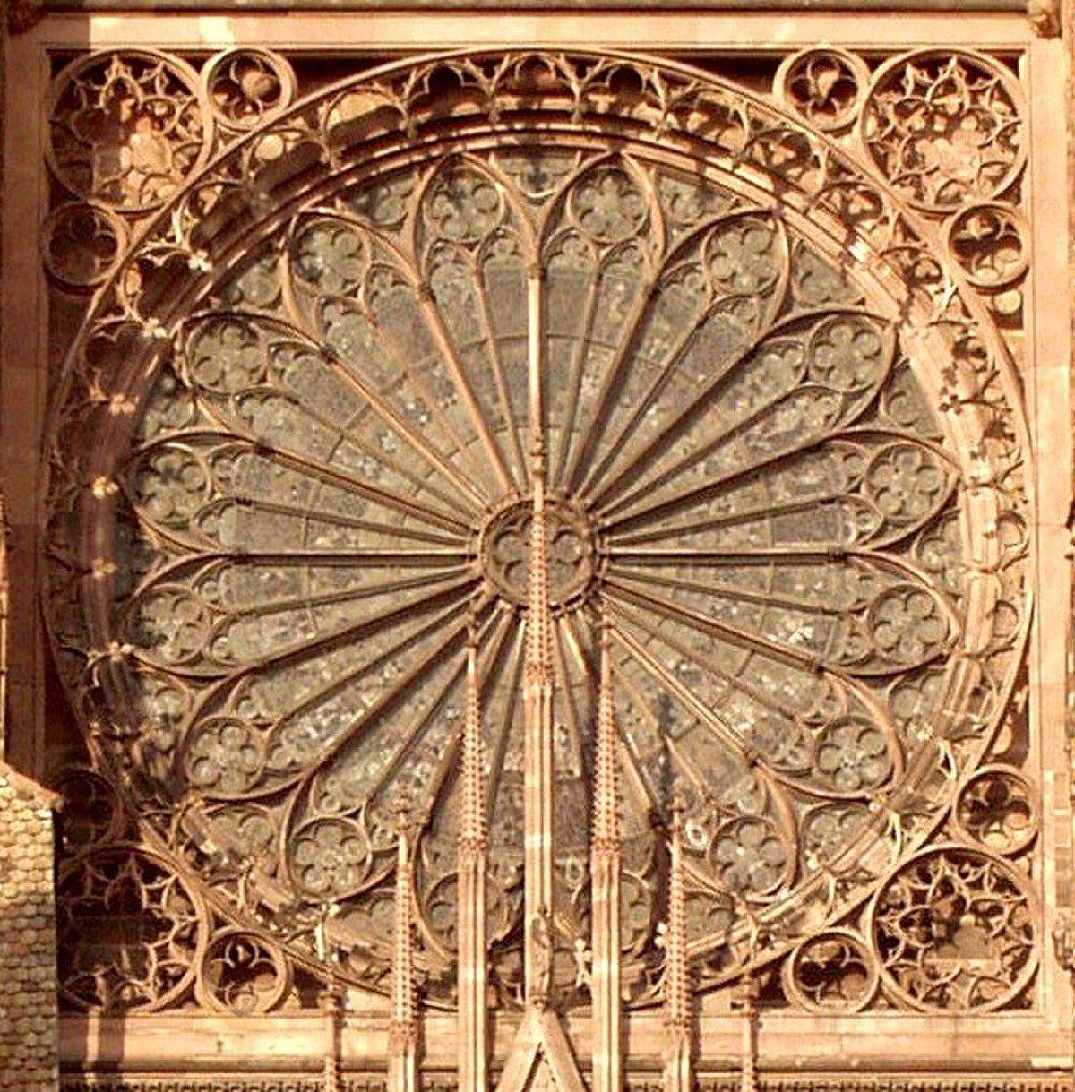 The exterior of the rose window at Strasbourg Cathedral in France is shown, featuring elaborate stone tracery. The large circular window is framed by intricate carvings and smaller decorative rosettes, with architectural elements of the cathedral visible below.