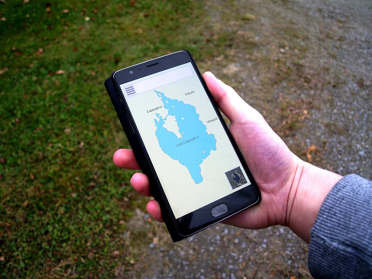 A smartphone displaying a web map application showing Lake Lappajärvi in Finland. The phone is held in a hand, with a green grassy background.