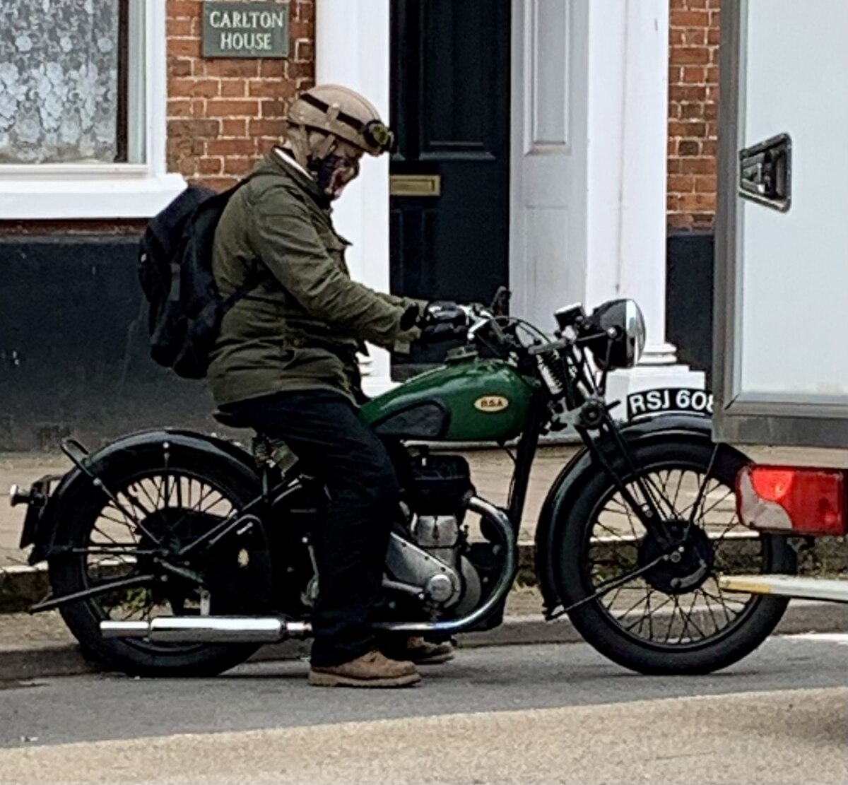 A person in vintage clothing sits astride a green vintage BSA motorcycle on High Street in Honiton, England, in July 2023.