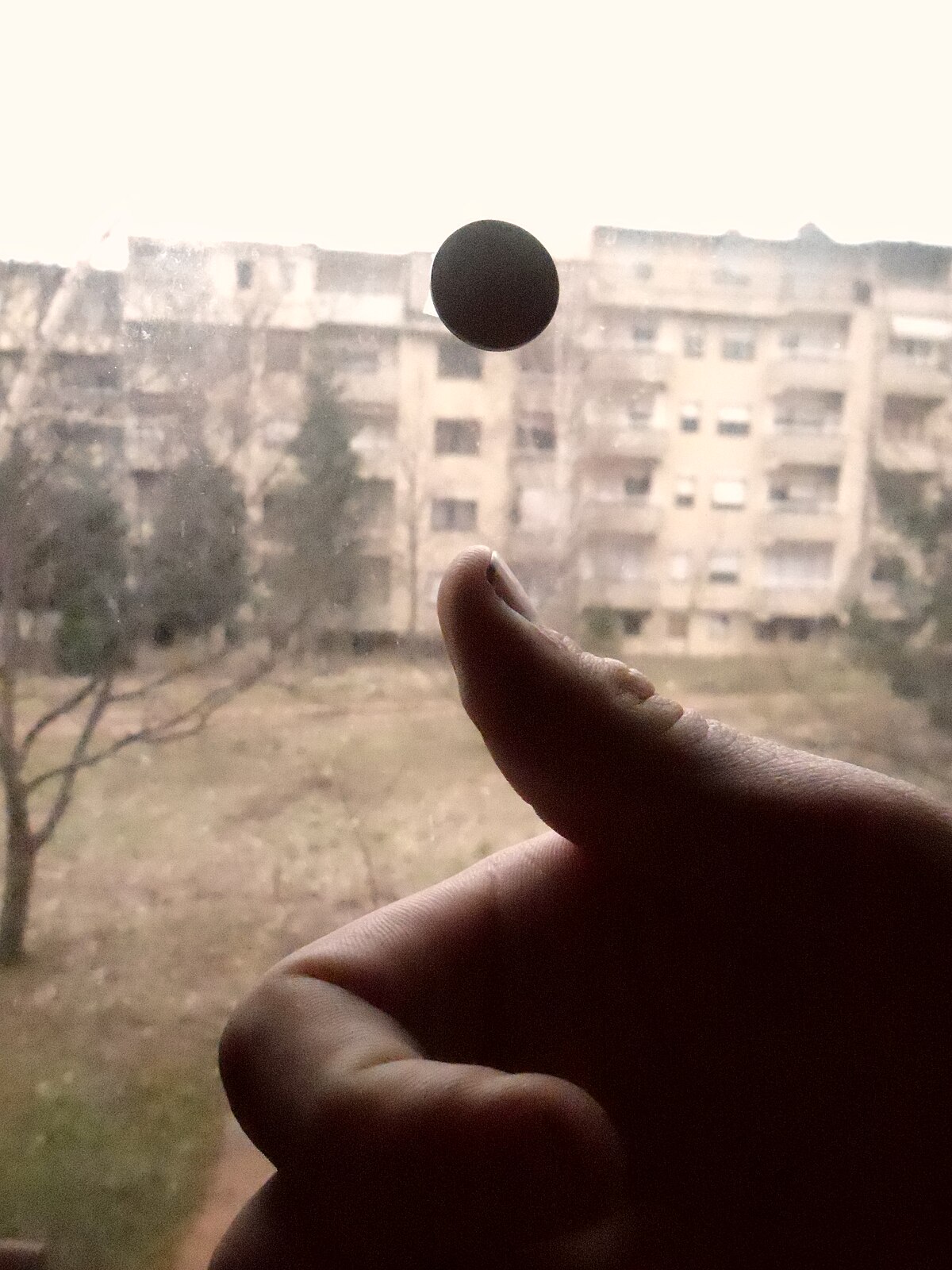 A hand flipping a coin into the air, with a blurred background of buildings and trees. The coin is suspended in mid-air above the thumb.