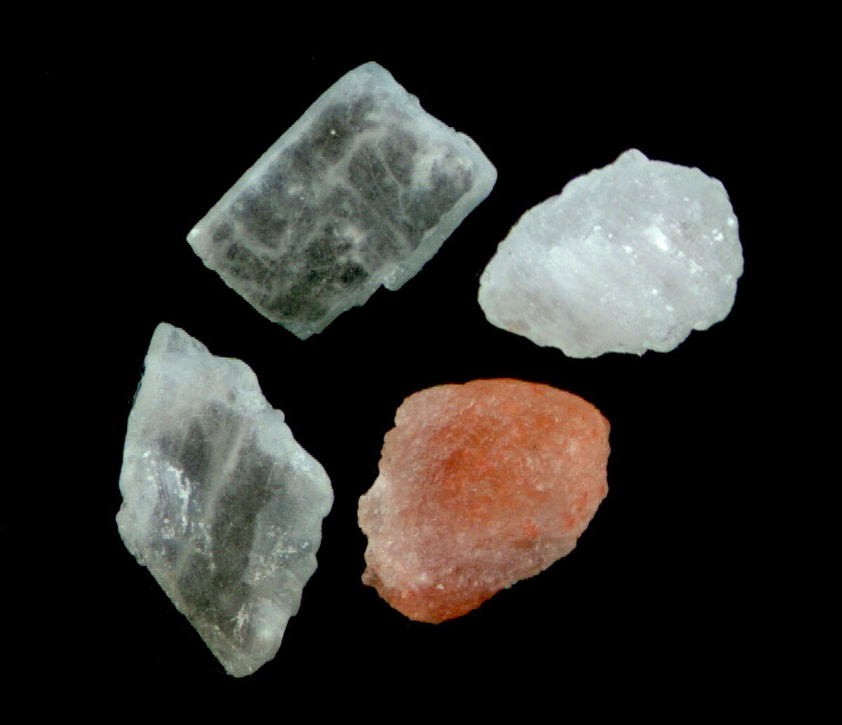 Four Himalayan salt crystals of varying colors, including clear, white, and reddish-orange, displayed against a black background. The crystals show different textures and translucencies.