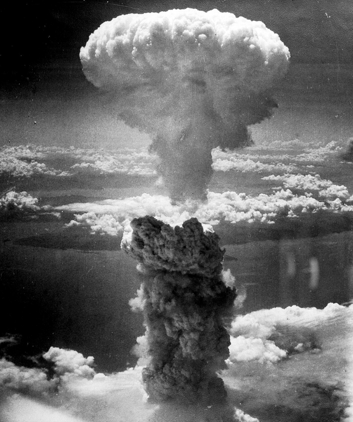 A massive mushroom cloud rises over Nagasaki, Japan, following the atomic bombing on August 9, 1945. The cloud extends high into the atmosphere, with a smaller, denser cloud forming closer to the ground.