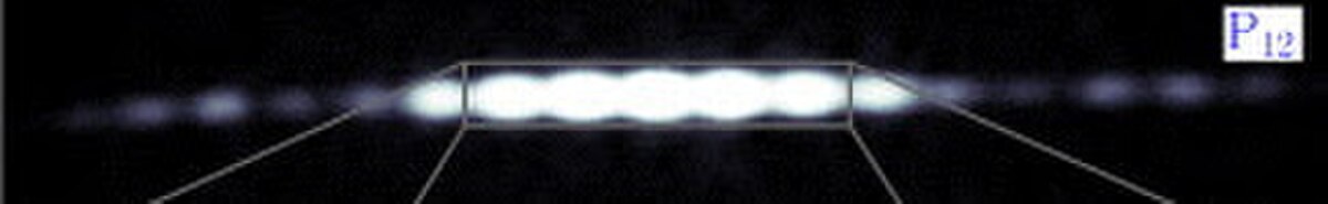 A close-up image of an electron interference pattern, labeled P12, showing distinct bright and dark fringes, characteristic of wave interference.