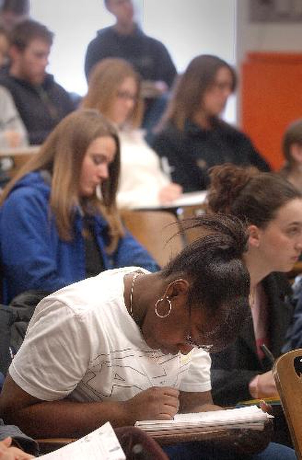 Students at the School of Veterinary Medicine at the University of Wisconsin–Madison are shown taking notes during a classroom lecture in June 2005. The foreground shows a student with dark hair writing in a notebook, while other students are visible in the background.