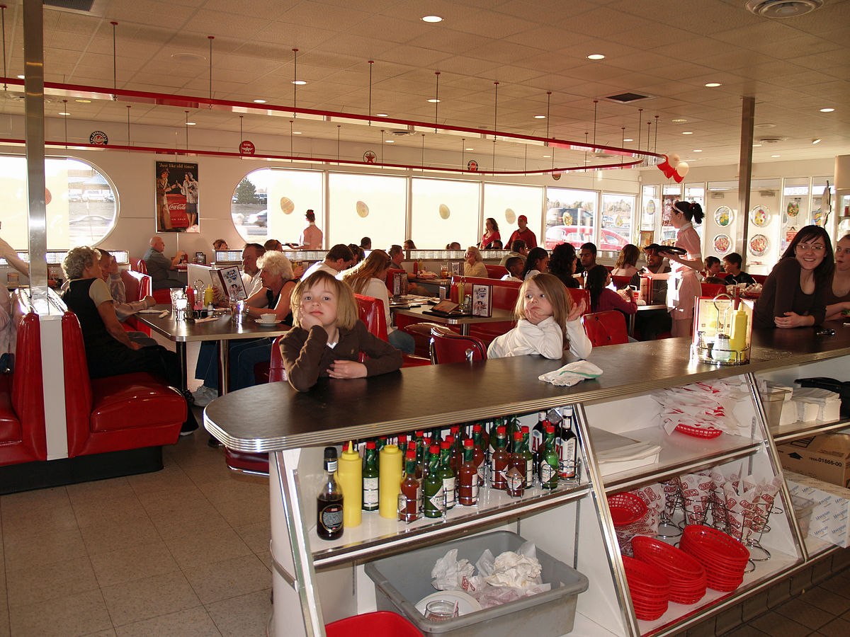 The interior of Ruby's Diner in Colorado Springs, 2008, features a classic 1950s-style decor with red booths, a long counter, and checkered flooring. Numerous patrons, including two young children in the foreground, are seated throughout the restaurant.
