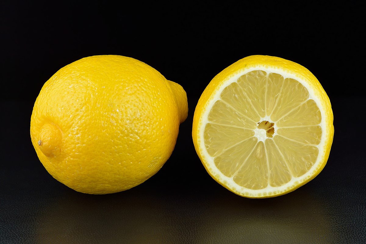 A whole lemon and a half-cut lemon are displayed against a black background. The cut lemon reveals its internal structure, including segments and seeds.