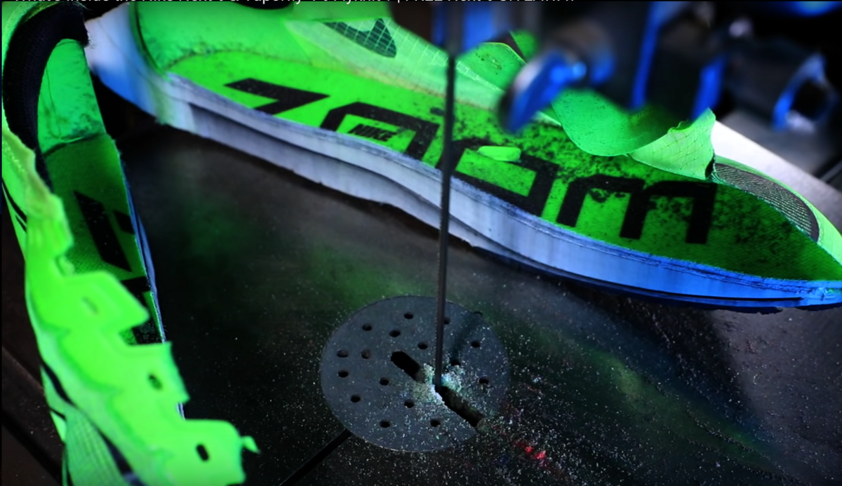 A Nike Vaporfly running shoe cut in half by a saw, revealing the internal layers of the sole. The shoe is bright green with "ZOOM" branding, and a dark grey line indicates the carbon fiber plate within the sole.
