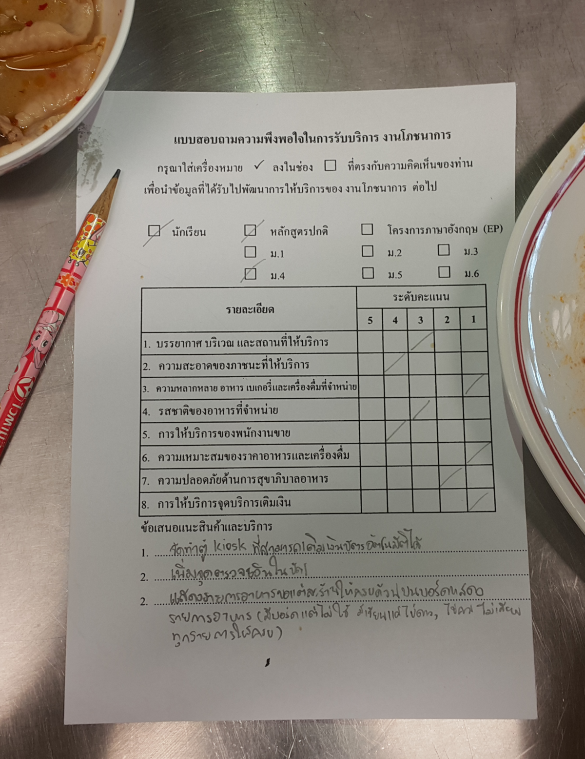 A basic questionnaire in the Thai language, partially filled out with pencil, resting on a table next to a bowl. The questionnaire includes sections for "แบบสอบถามความพึงพอใจในการบริการ งานโภชนาการ" (Satisfaction Survey for Food Services) and a rating scale from 1 to 5 for various service aspects.