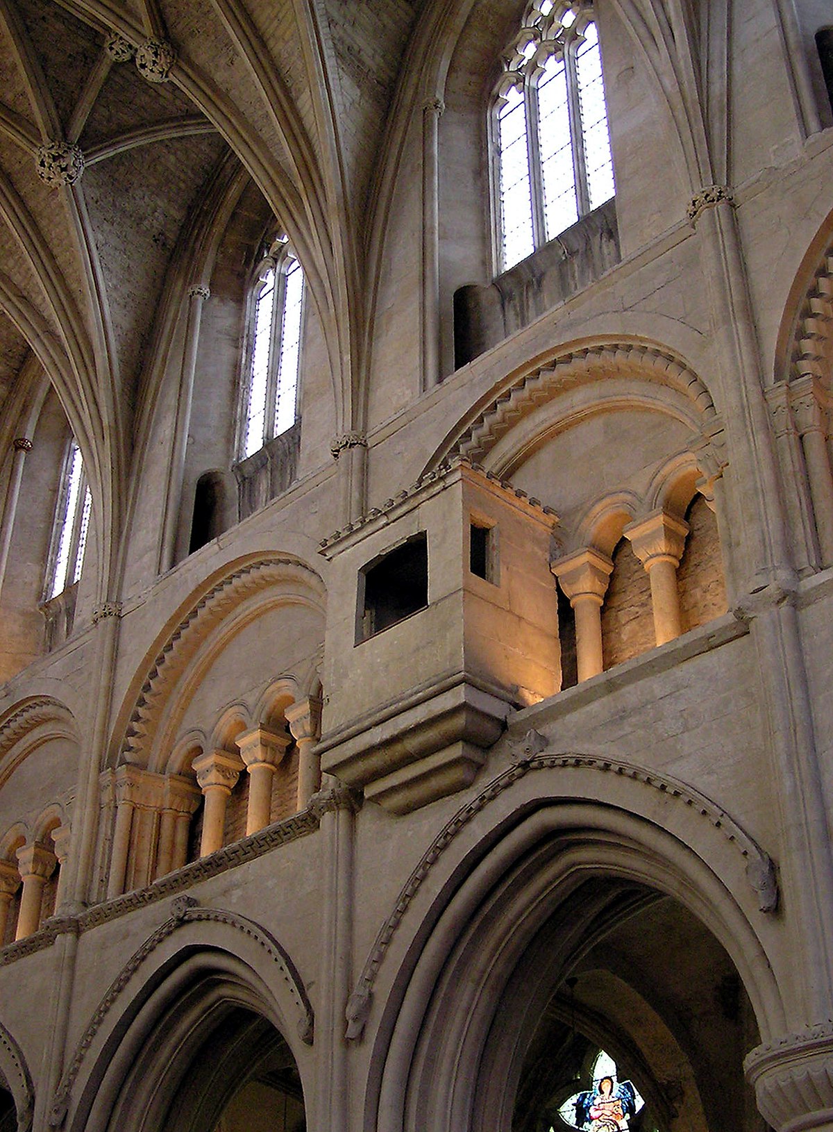 The nave wall of Malmesbury Abbey in Wiltshire, England, divided into three stages: the clerestory with windows at the top, the triforium beneath it, and the arcade at the lowest stage. The Romanesque architecture features rounded arches and intricate stone carvings.
