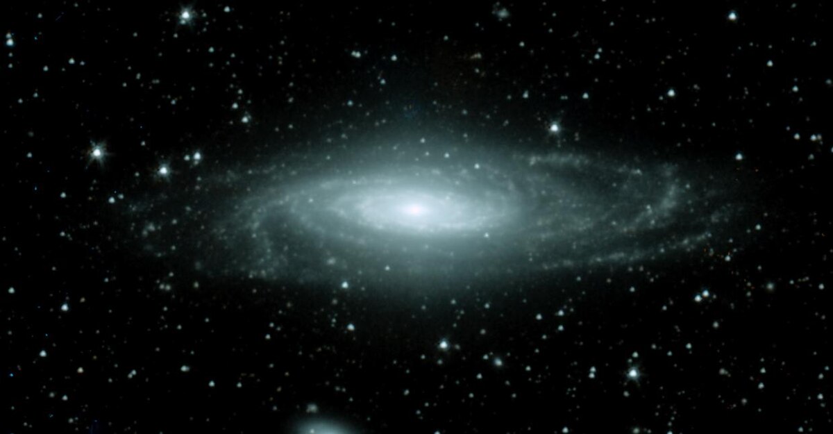 A spiral galaxy, NGC 7331, seen nearly edge-on, with a bright central bulge and distinct spiral arms visible against a dark, star-filled background. The galaxy's light appears bluish-white, indicating active star formation.