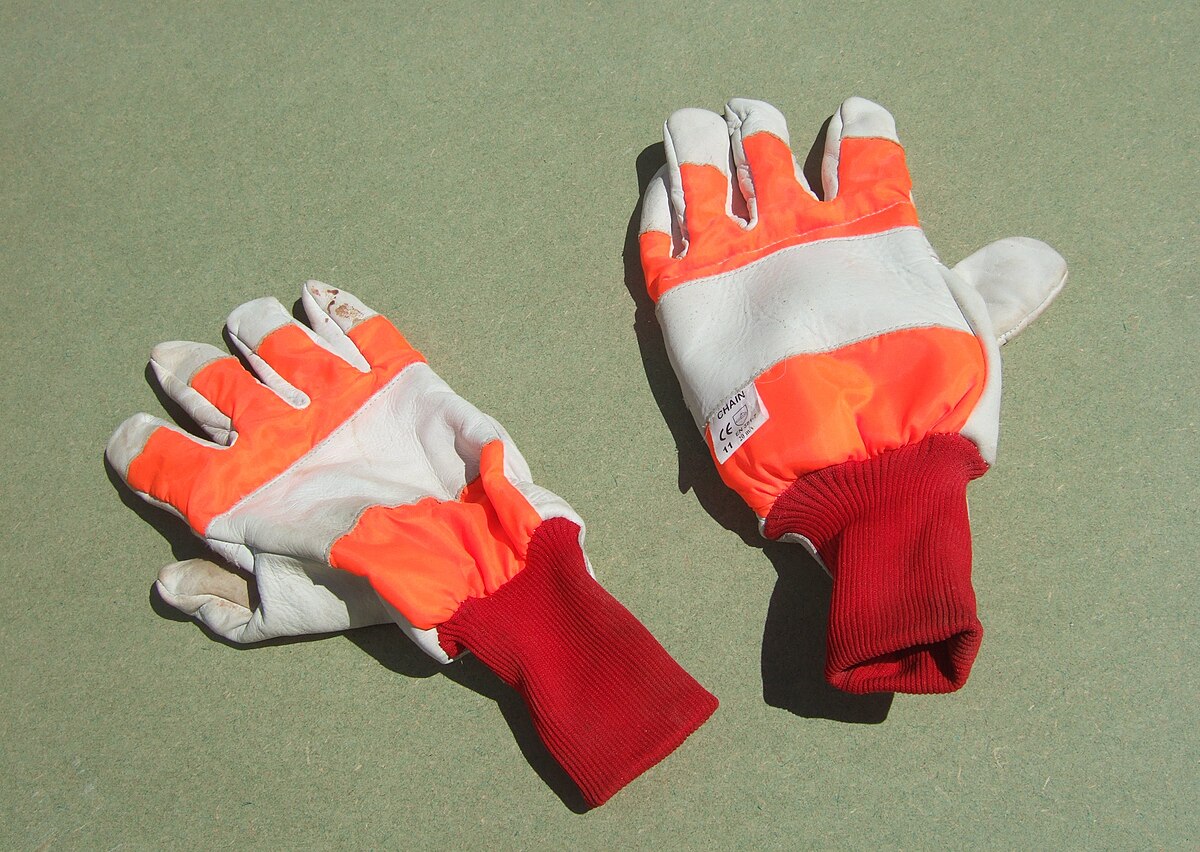 A pair of chainsaw gloves, with the left glove featuring orange protective fabric on the back and a chainsaw safety label. The right glove is primarily white with orange accents and lacks the protective fabric and label.