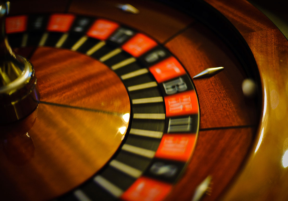 A close-up shot of a roulette wheel in motion, with the ball resting in a numbered slot. The wheel features red and black numbered pockets.
