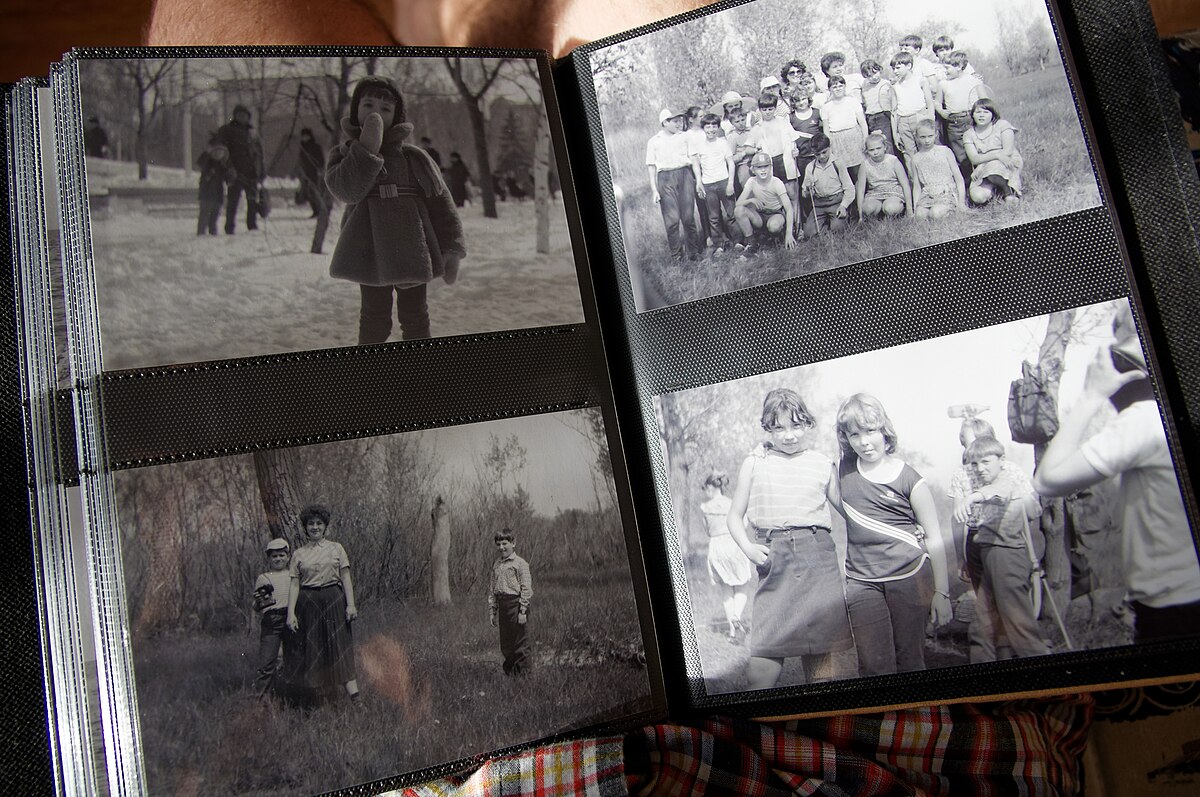 An open photo album displays several black and white photographs, primarily featuring children and groups of people. The images capture candid moments outdoors, suggesting family or school memories from Rostov-on-Don, Russia.