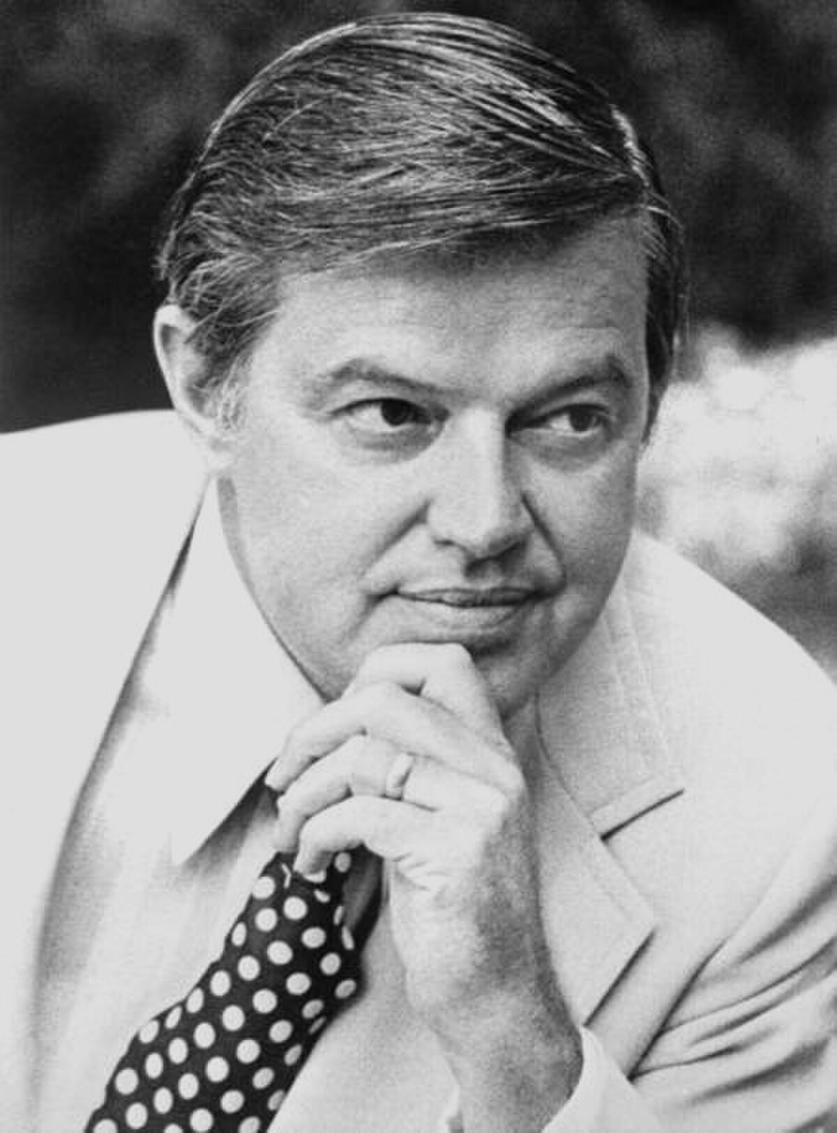 Portrait of Frank Church, who headed the Church Committee investigation into U.S. intelligence agencies. He is looking to the right, with his hand on his chin, wearing a light-colored suit and a polka-dot tie.