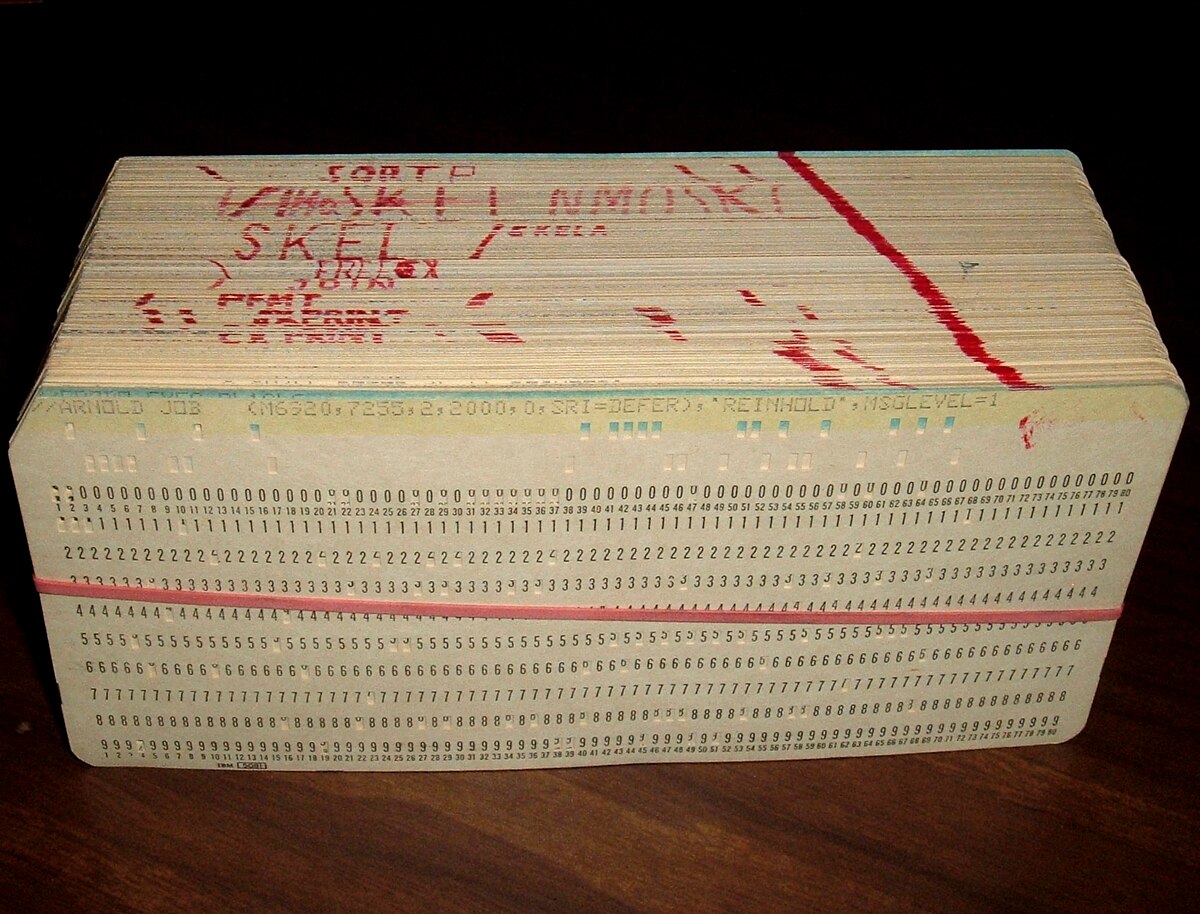 A deck of punched cards, comprising a computer program, is bound together with a red rubber band. A red diagonal line is marked across the top edges of the cards, serving as a visual aid to keep the deck sorted.