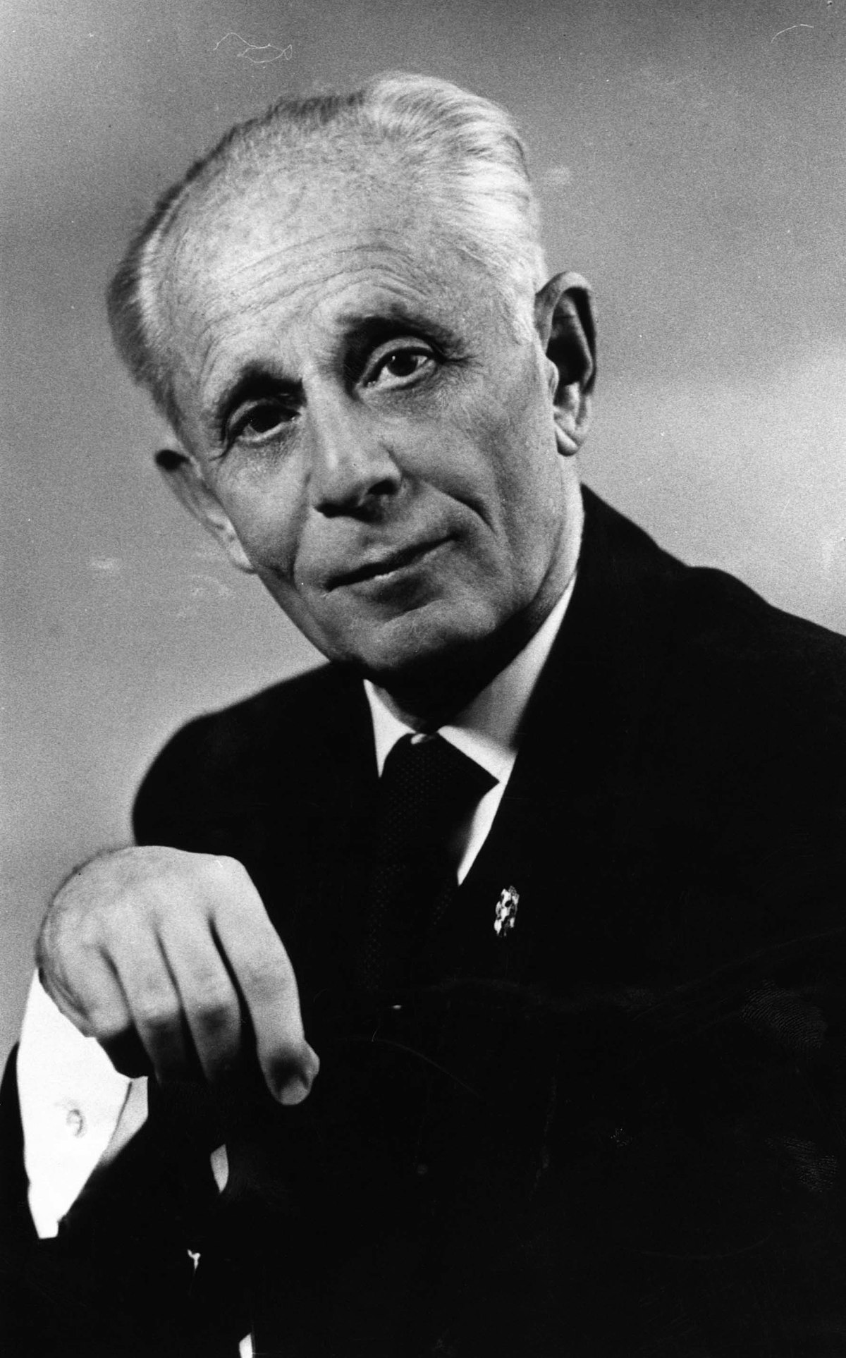A black and white portrait of Hans Selye shows him looking towards the viewer, wearing a suit and tie. He has a serious expression and is holding his hand to his chin.