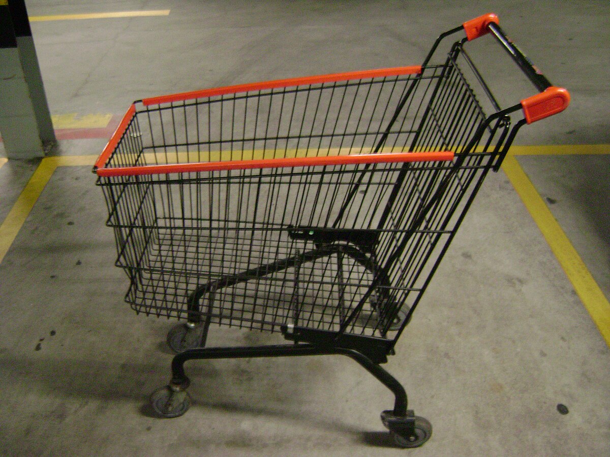 A black wire shopping cart with orange plastic handles and trim is parked on a concrete floor with yellow painted lines.