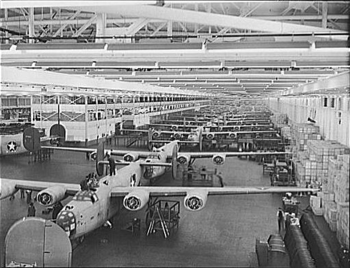 A wide shot of the Ford Motor Company's Willow Run factory during World War II, showing numerous B-24 Liberator military aircraft in various stages of assembly on a vast production floor.