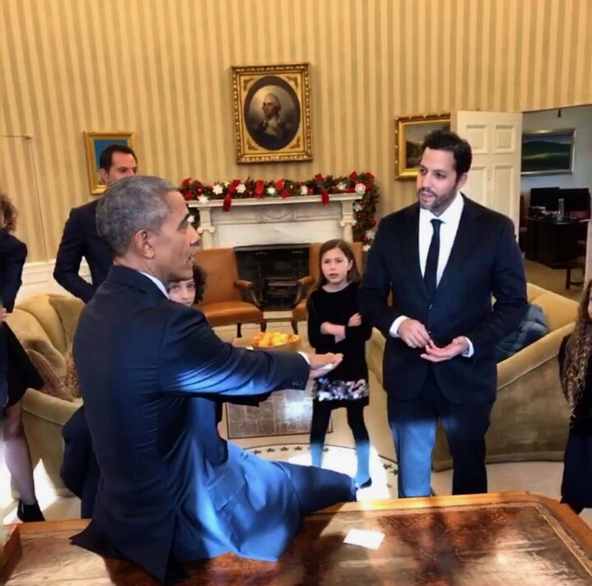 Illusionist David Blaine performs magic for President Barack Obama at the White House in 2016. Blaine stands opposite Obama, who is seated at a table, with other people including children observing in the background.