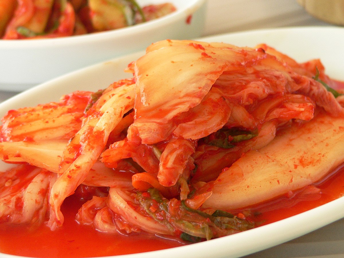 A close-up of Kimchi, a common Korean side dish, showing vibrant red, spicy fermented cabbage on a white rectangular plate.