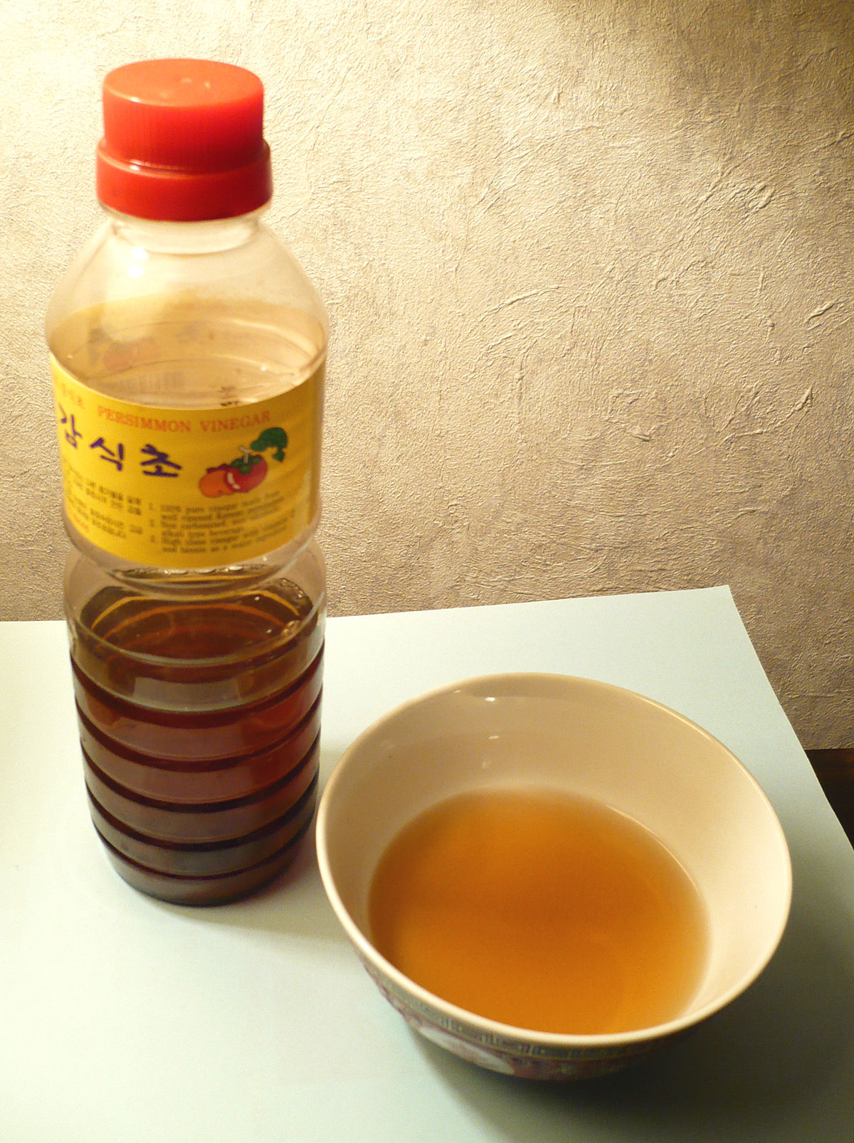 A bottle of persimmon vinegar produced in South Korea, labeled in Korean as "감식초" (Gam-sikcho), next to a bowl containing a serving of the amber-colored vinegar.