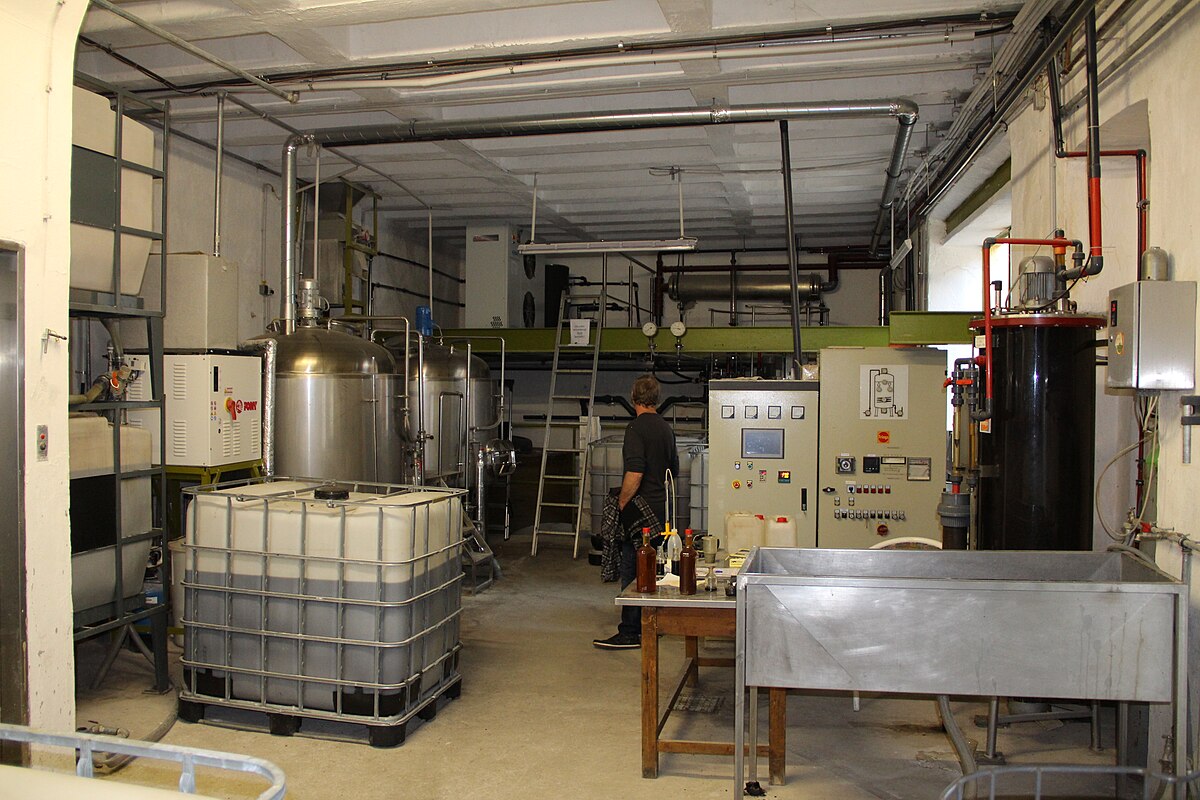 An industrial facility with fast aerobic fermentation stainless steel vessels used for vinegar production. A person is visible working among the machinery, tanks, and control panels.