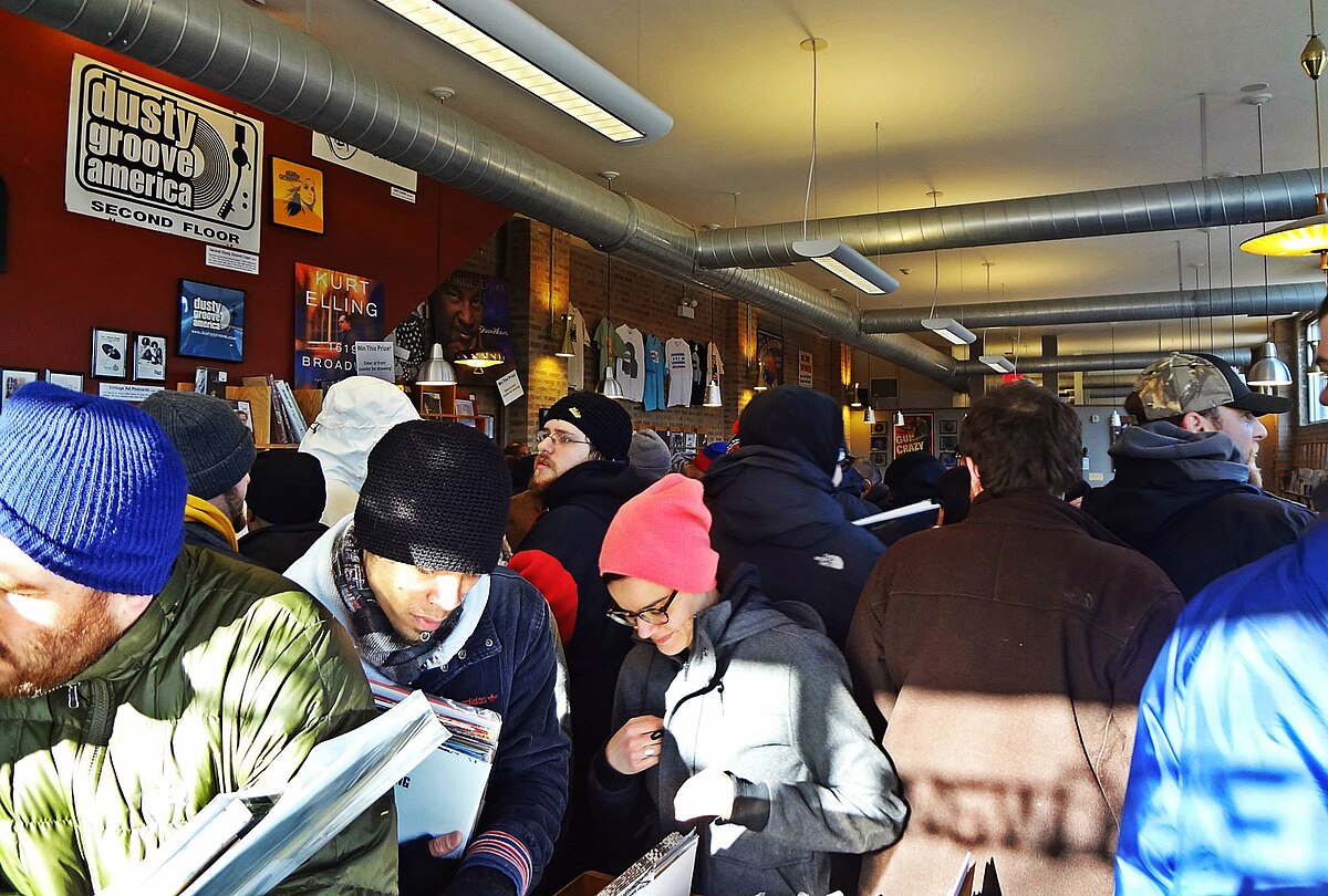 A crowd of people browse records inside the Dusty Groove store during Record Store Day in April 2014. Shoppers are seen looking through bins of vinyl records in the busy store.