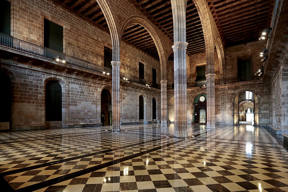 The interior of the Llotja de Barcelona, where the city's Taula de canvi operated, features a grand hall with a checkered floor and tall arched ceilings supported by numerous columns. Sunlight reflects off the polished floor, highlighting the architectural details.