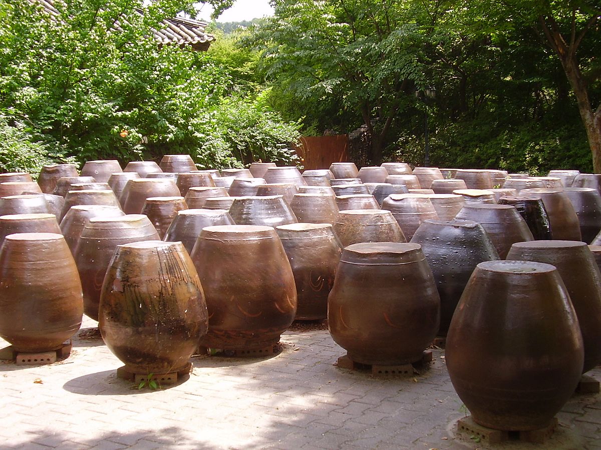 Numerous traditional Korean earthenware jars, called onggi, are arranged outdoors. These jars are used for storing fermented foods like kimchi, gochujang, doenjang, and soy sauce.