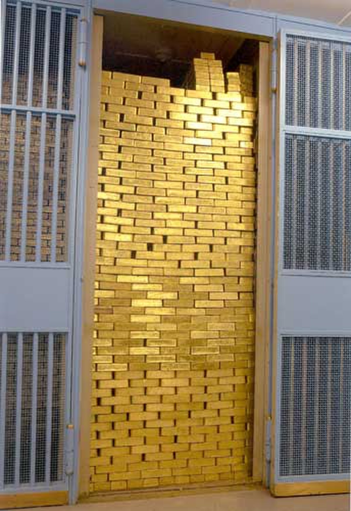 A gold compartment at the Federal Reserve Bank of New York is filled with stacks of gold bars, reaching almost to the ceiling. The gold is visible through the open door of a barred vault.