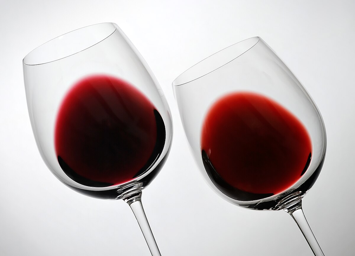Two wine glasses filled with red wine, demonstrating the color difference due to oak aging. The wine on the left is a two-year-old cosecha, and the wine on the right is a six-year-old crianza, showing a shift from deep purple to a lighter brick-red.