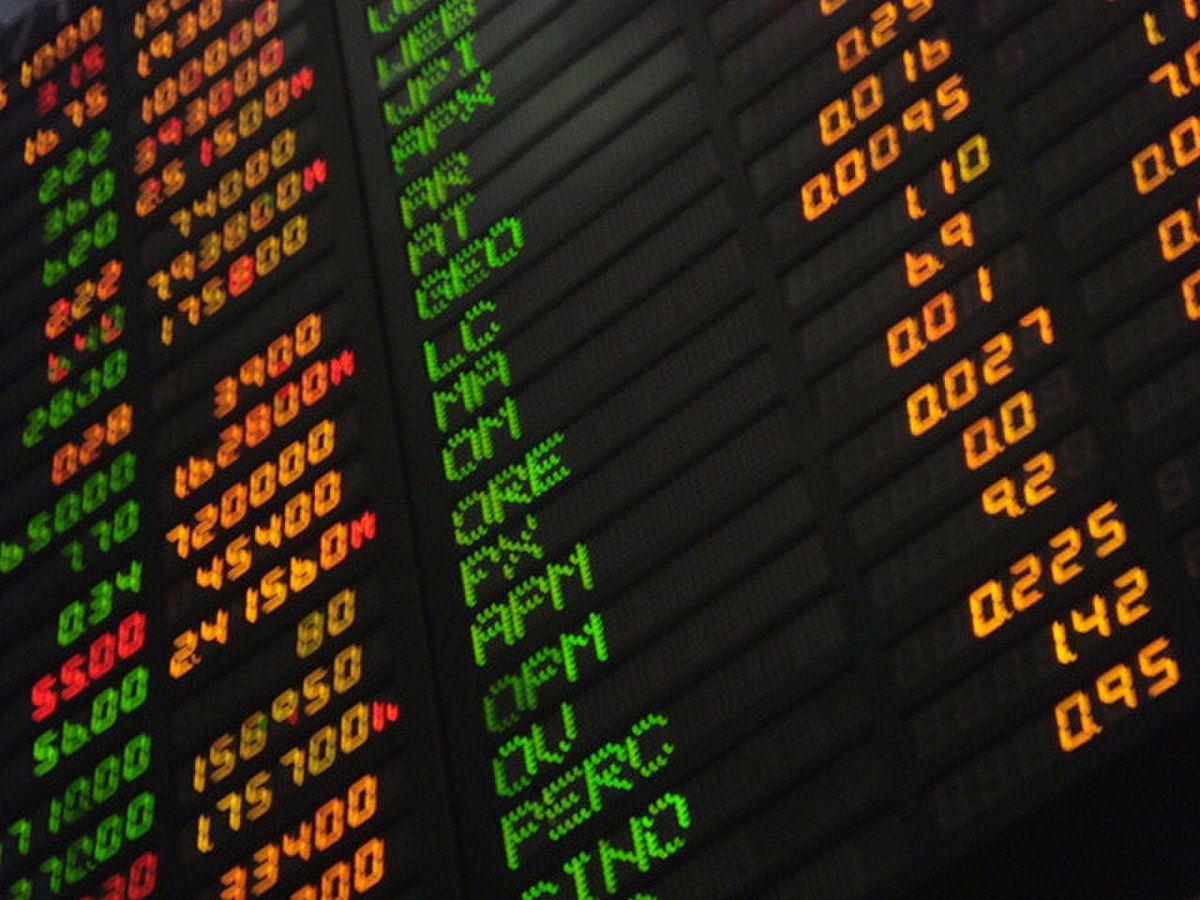 Close-up of a Philippine stock market board displaying various stock tickers and numerical data in green, red, and orange LED lights. Visible tickers include "JGS", "APN", "GEO", "LC", "MA", "ORE", "APM", "OU", "PERC", and "SINO", alongside corresponding numerical values representing prices or changes.