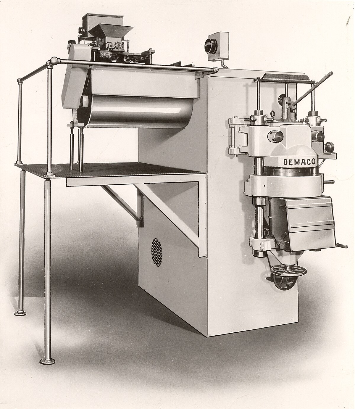 A black and white photograph from 1958 shows a DEMACO 1,000 lbs/hr short goods pasta press, a non-vacuum extruder. The large industrial machine features various gears, levers, and a hopper for raw ingredients.