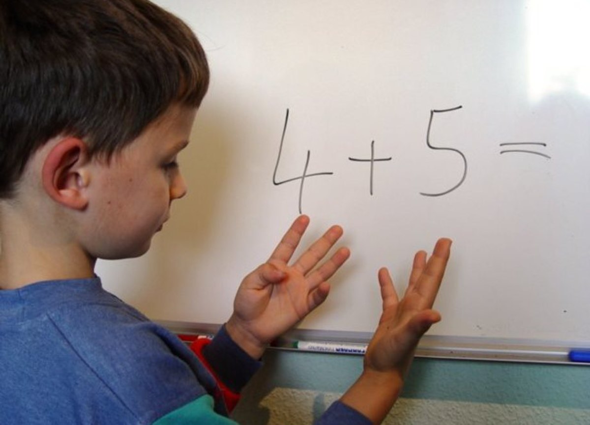 A young boy calculates with his fingers while looking at the equation "4 + 5 =" written on a whiteboard. He is using his fingers to count, demonstrating a concrete method for solving addition problems.