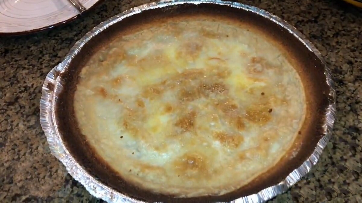 A homemade water pie is shown in a foil pie pan, featuring a light-colored, slightly browned top crust with some darker spots.