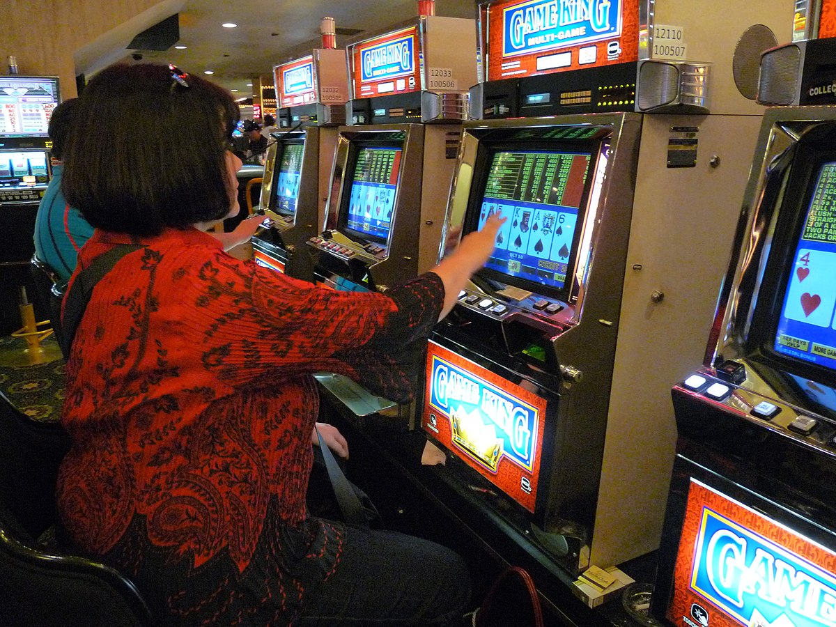 A woman is seated at a row of slot machines in the Imperial Palace casino in Las Vegas, playing a video poker game. The screens display card hands, and the machines have various buttons and lights.