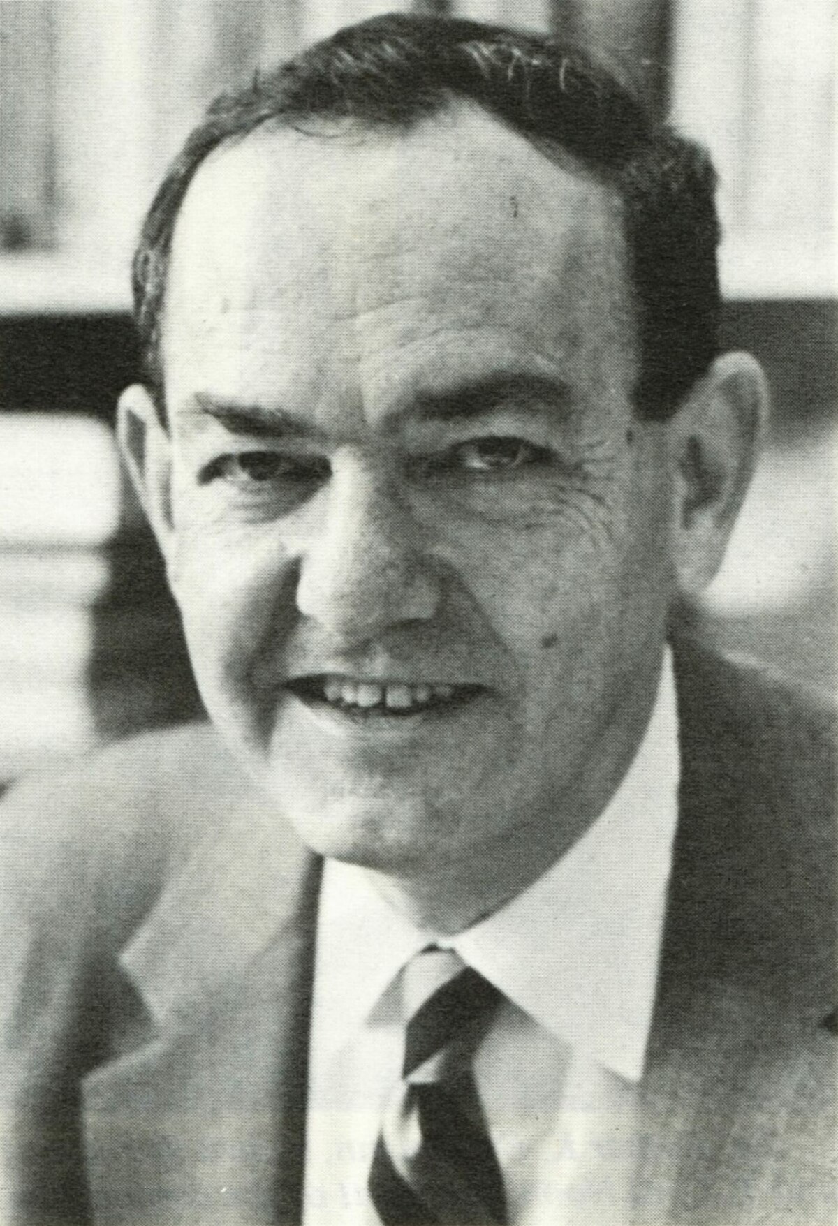 A black and white portrait of Herbert A. Simon, an American economist, political scientist, and cognitive psychologist. He is shown smiling slightly, wearing a suit and tie.