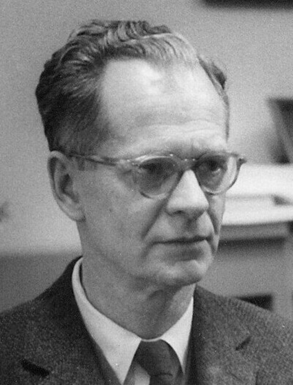 Black and white portrait of B. F. Skinner, a man with short, neatly combed hair, wearing glasses, a suit jacket, and a tie. He is looking slightly to the right of the viewer.