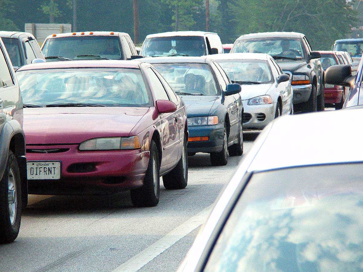 A traffic jam in Baltimore, Maryland, shows multiple cars bumper-to-bumper on a highway. The license plate of a red car in the foreground reads "DIFRNT".