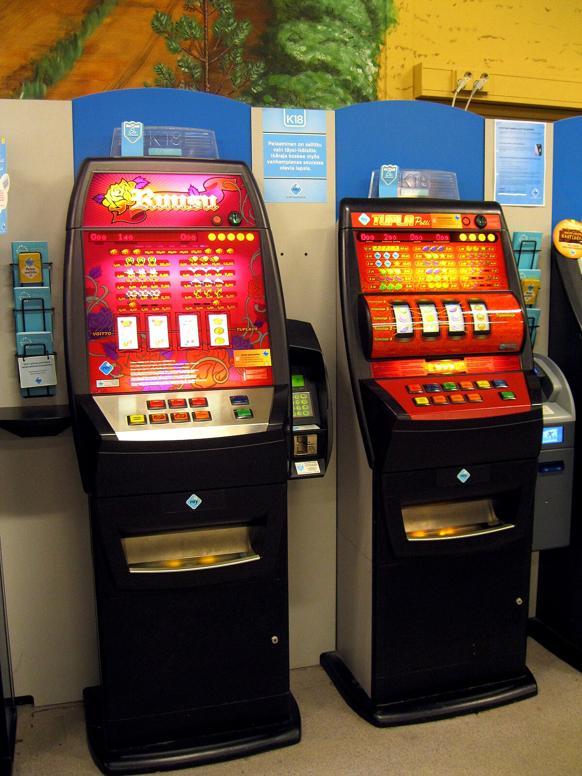 Two RAY slot machines, named Ruusu and Tuplapotti, are displayed in Finland. The machines have colorful, illuminated screens with various game symbols and buttons for playing.