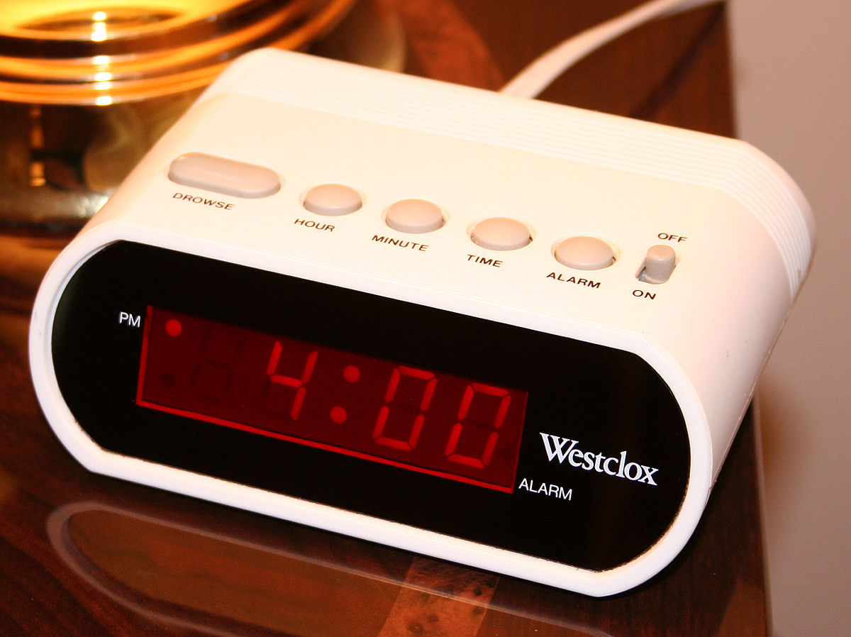A white Westclox digital alarm clock with a red LED display shows the time "4:00" with a "PM" indicator in the top left corner. Buttons on top include "DROWSY," "HOUR," "MINUTE," "TIME," and "ALARM ON/OFF."