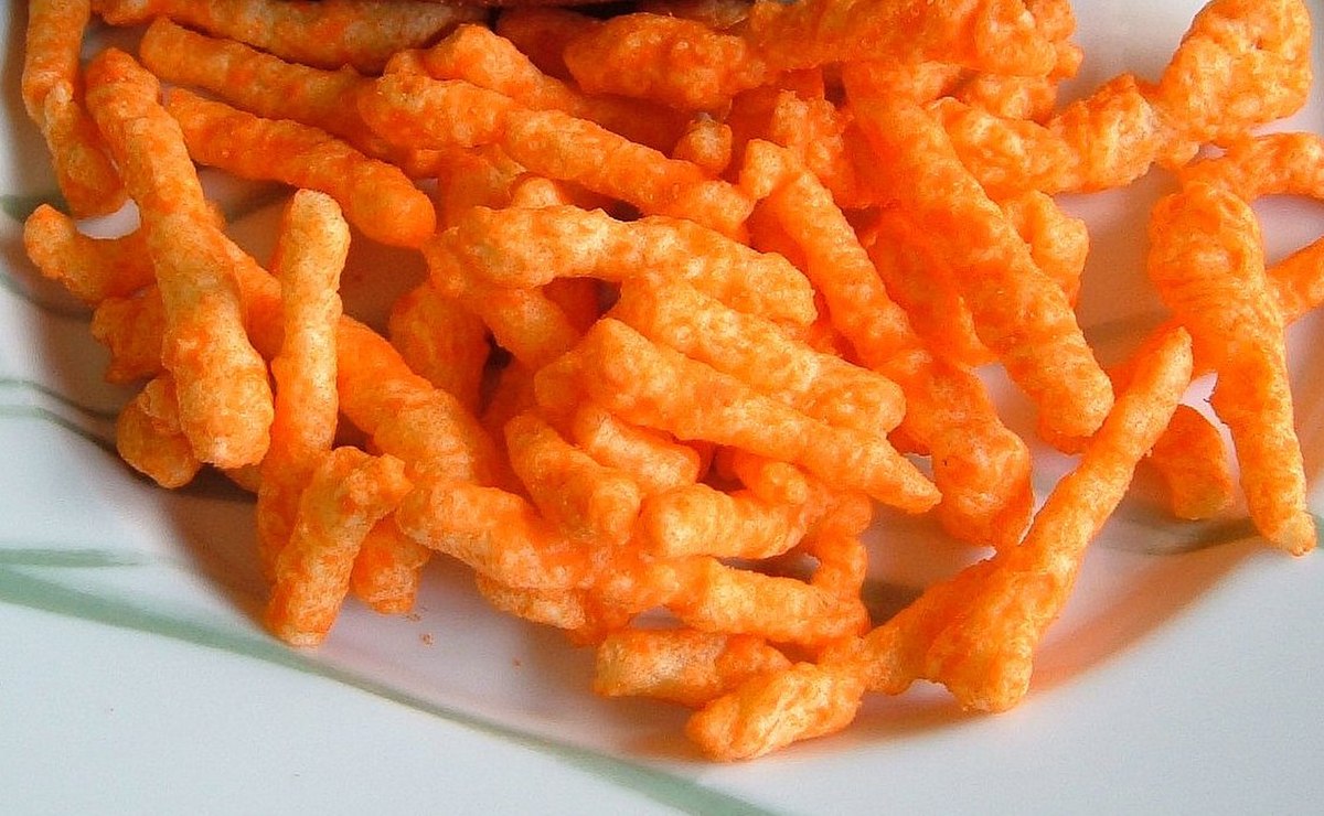 A close-up view of Cheetos Crunchy cheese-flavored snacks piled on a white plate with a green decorative edge.