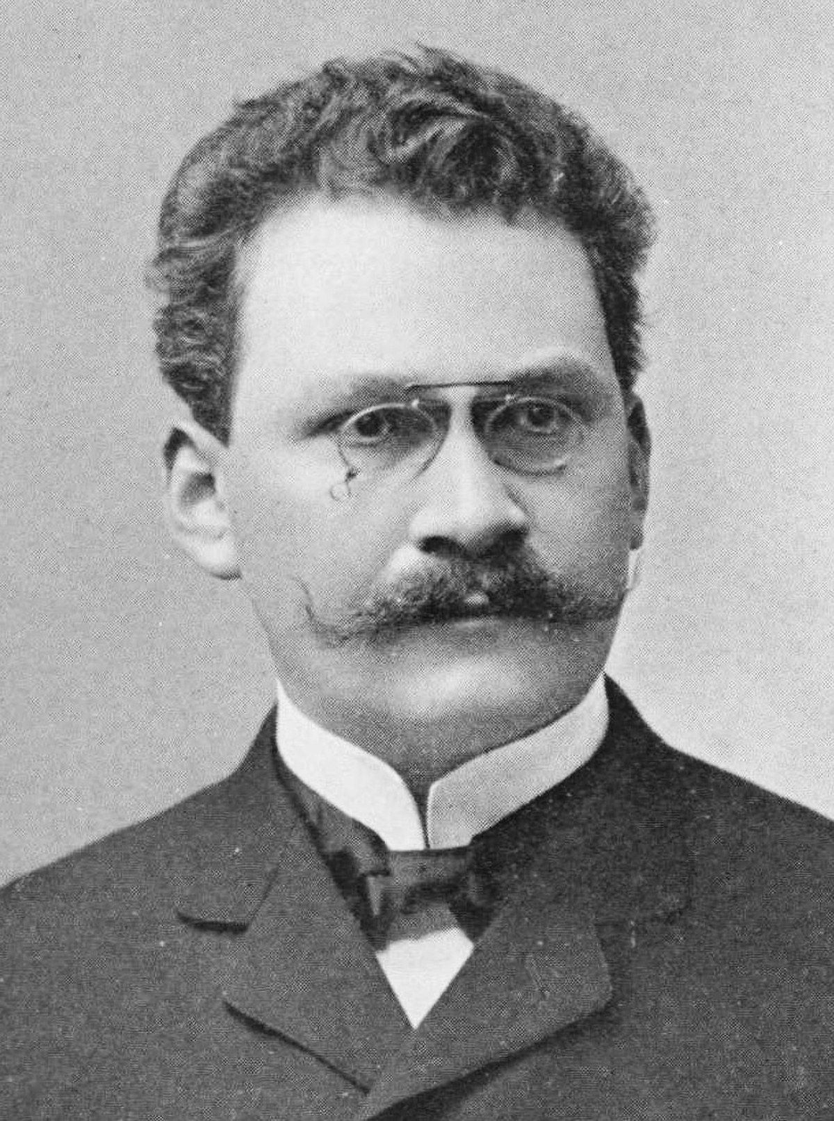 Black and white portrait of Hermann Minkowski, a German mathematician and physicist. He is shown with a mustache and pince-nez glasses, wearing a suit jacket and tie.